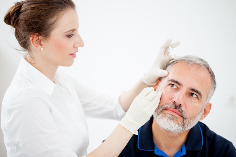Stock photograph of models: a gloved doctor examines the cheek of a grey-bearded man