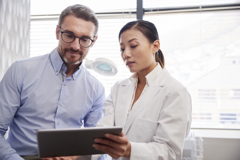 Stock photograph of models: a doctor in a white coat shows a tablet to a man in glasses