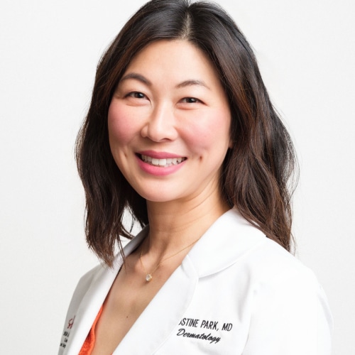 Dr. Justine Park, smiling, in a white coat embroidered with her name